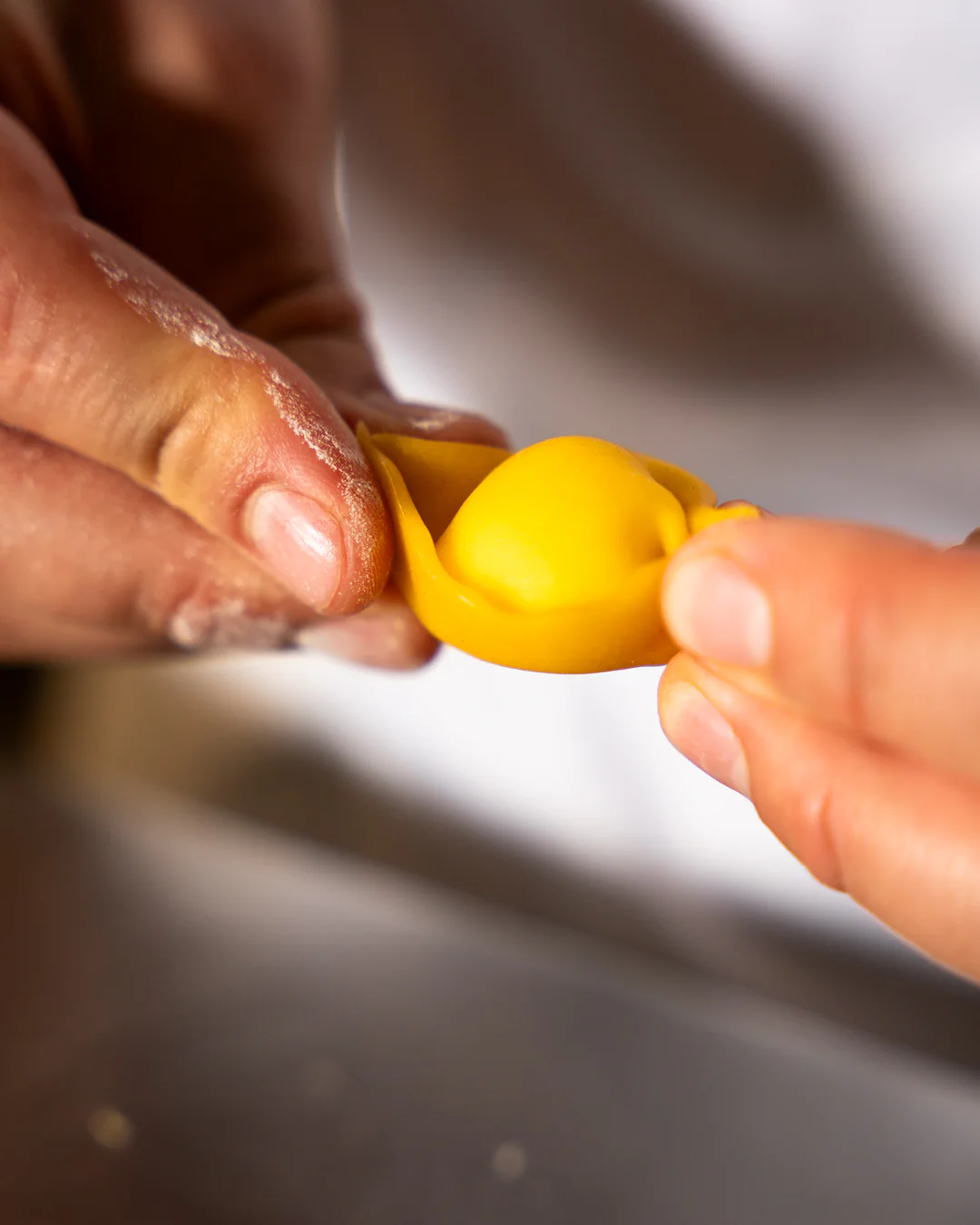 Le mani che chiudono un tortello di pasta fresca