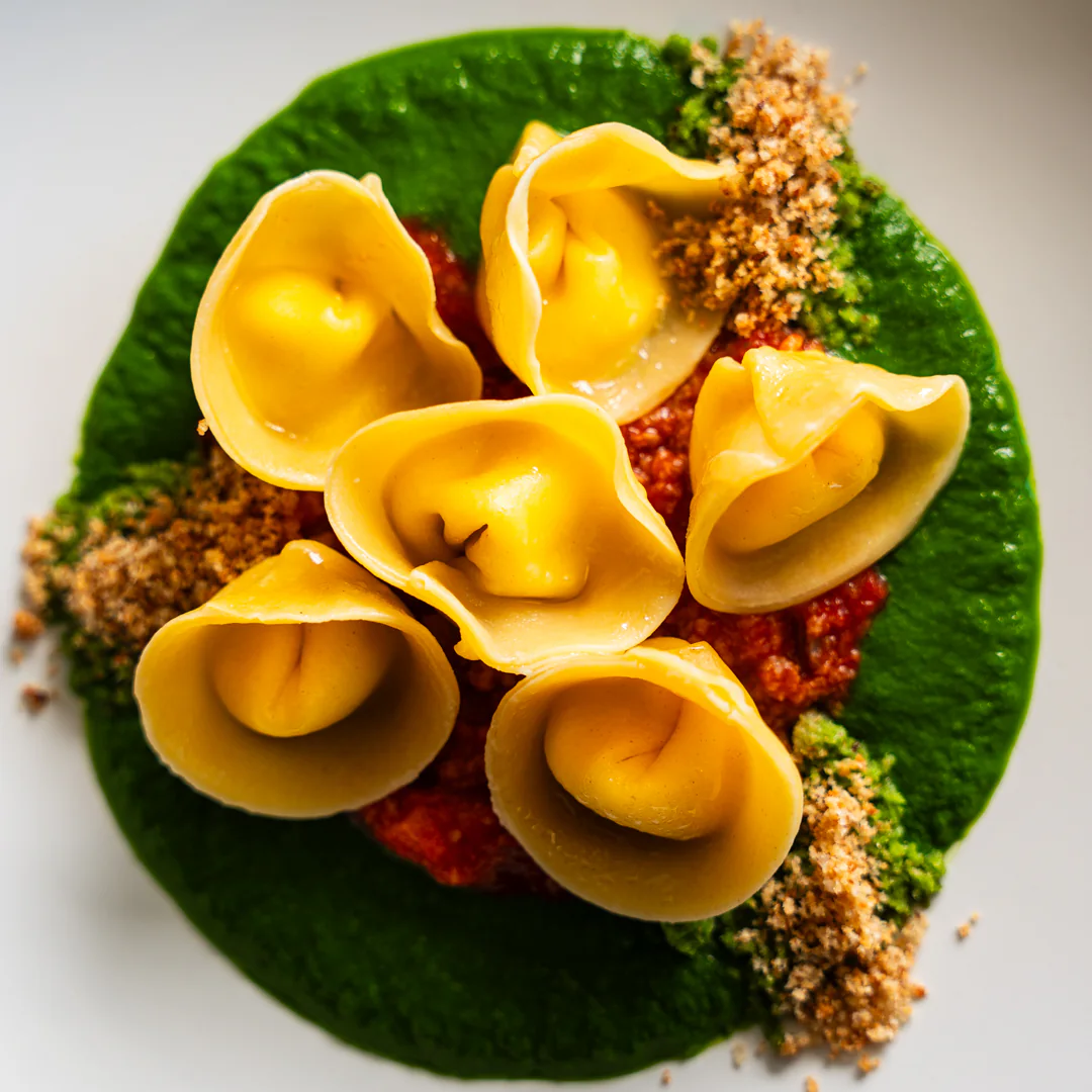 Tortelli di pasta fresca in farcia di ricotta, ragù di conchigliacei, crema di cavolo nero e mollica atturrata