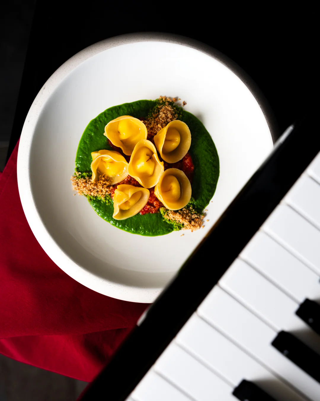 Tortelli di ricotta su crema di cavolo nero accanto ai tasti di un pianoforte